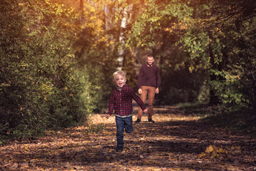 Fototapeta na wymiar Blond boy runs away from his father. Autumn forest. Happy childhood.