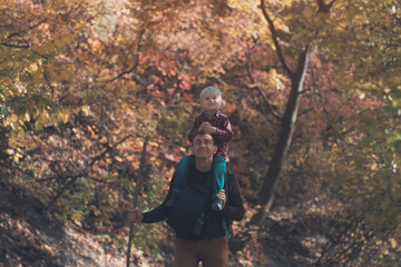 Father with son on his shoulders walking in the autumn forest. Back view