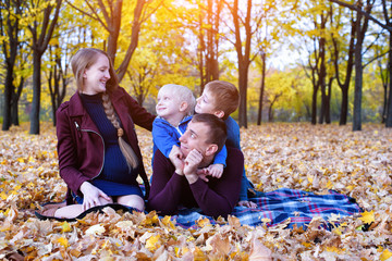 Parents and two sons relax and chat in the park. Pregnant mom Happy family. Yellow autumn foliage, sunny day