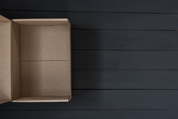 Empty open cardboard box on black wooden background. Delivery concept. Top view