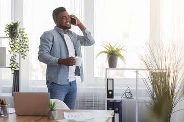 Businessman with coffee and cellphone standing near window in office