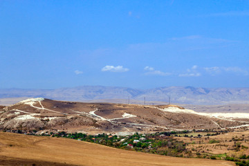 Sunny valley with yellow grass, mountains and white clouds on blue sky.