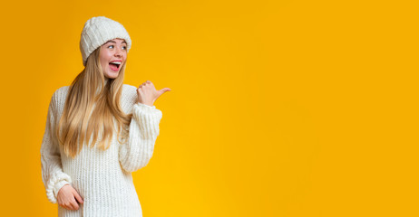Cheerful girl pointing with thumb at empty space