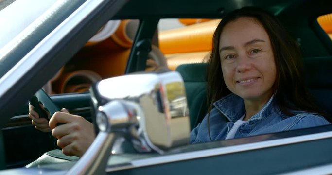 adult smiling brunette woman is sitting on driving-seat inside old rarity auto