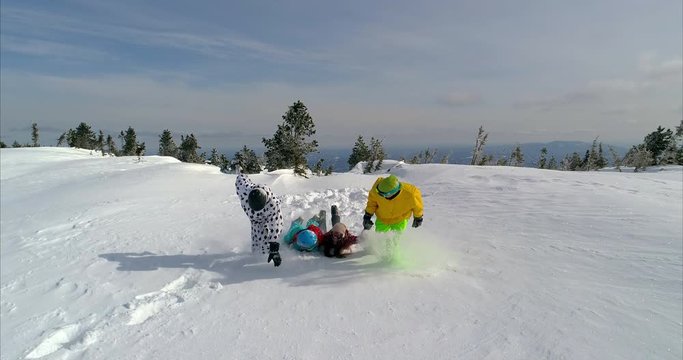 SLOW MO: a team of youngsters in bright snowboard suits are holding hands and running through the deep snow with a fall at the end. team play at the ski resort, team building and willpower. front view