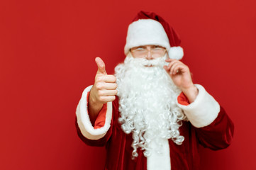 Close-up photo of Santa Claus's hand shows thumb up, man looks into camera and smiles, focus on hand with liking gesture. Isolated. Smiling Santa shows thumb up. Christmas. Xmas concept