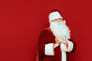 Portrait of happy Santa Claus standing with bag of gifts on his back on red background, looking into camera and smiling. Christmas gifts and positive Santa isolated on red. Empty space. Copyspace