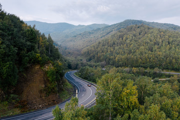 Aerial view of a sharp turn on a mountain road among green forest trees. Car traffic on a highway. P-258 road on the shore of Baikal Lake near Baikalsk, Buryatia, Russia