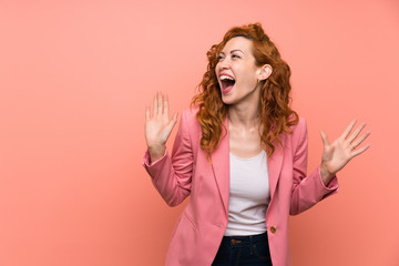 Redhead woman in suit over isolated pink wall with surprise facial expression