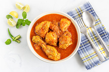 Indian Chicken Curry in a Bowl with Fork and Spoon on White Background, Garnished with Mint Leaves and Lemon Directly .Above Photo.