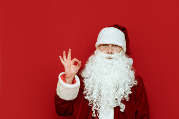 Santa Claus stands on a red background and shows his thumb gesture OK. Isolated. Santa and the gesture Okay. Christmas and New Year. Copyspace