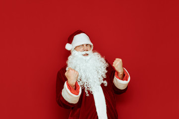 Portrait of Joyful Santa Claus rejoices in victory over red background. Santa is happy, yelling and actively gesturing with joy. Isolated. X-mas concept. Copyspace.