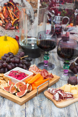 Plate with autumn snacks: beetroot dip , figs, grape, pumpkin, prosciutto, sausage, carrot and two colored glasses of red wine on rustic wooden background.