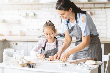 Mom and daughter making cookies together, pressing dough with cutter