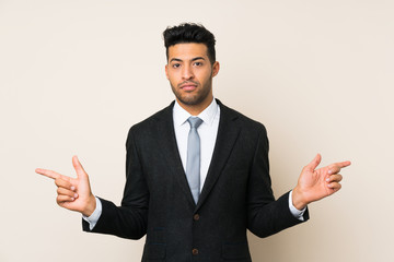 Young handsome businessman man over isolated background pointing to the laterals having doubts