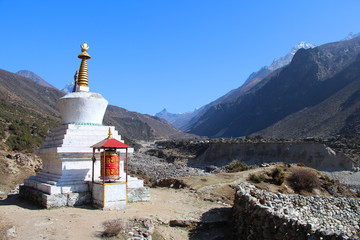 Old typical white Buddhist stupa (chorten) and red prayer wheel with repeating written buddhist...