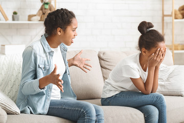 Little girl sitting on sofa crying, fighting with sister