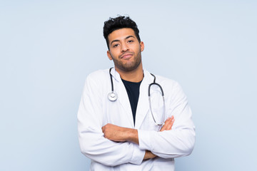 Young doctor man over isolated blue wall making doubts gesture while lifting the shoulders