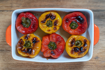 Baked red and yellow bell peppers. Peppers in a baking dish on a wooden table. A healthy and delicious vegetarian dish. Closeup, top view