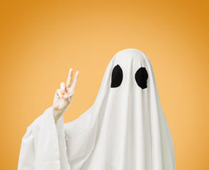 Halloween white ghost showing peace sign gesture on yellow background.