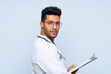 Young doctor man over isolated blue wall