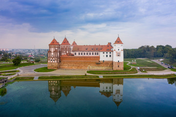 Naklejka na ściany i meble Mirsky Castle and its reflection in the lake in summer. Sunset in cloudy weather with rain clouds.