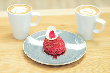 Close up a slice of red cake on the plate on the background of two cups of coffee. Piece of cake with cups of coffee on table at cafe.
