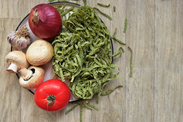 Raw fettuccine pasta with spinach on a plate with vegetables for the preparation of national Italian dishes. The concept of healthy eating. Vegetarianism, Keto diet. Copy space. Top view.