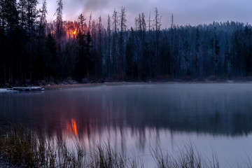 Forest fire burns in the woods above a beautiful mountain lake