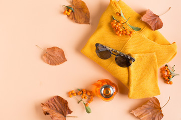 Autumn composition of sunglasses, brown leaves, a bottle of perfume and a yellow sweater top view copy space