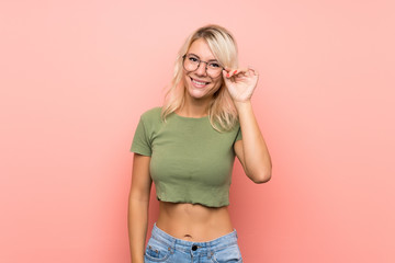 Young blonde woman over isolated pink background with glasses and happy