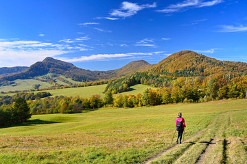 Fototapeta na wymiar Woman backpacker on hiking trail in the mountains in autumn sunny day