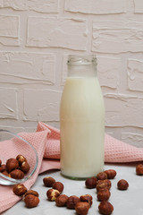 Bottle of non-dairy hazelnut milk with hazelnuts on grey background