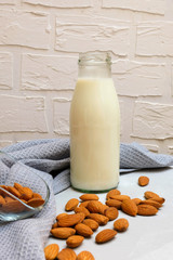 Bottle of almond milk with some almonds on grey bakround