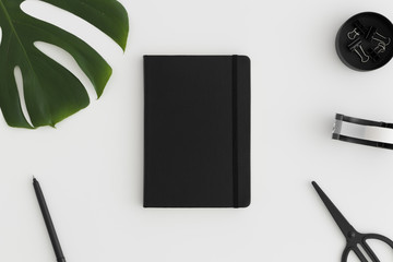 Black notebook mockup with workspace accessories on a white table.