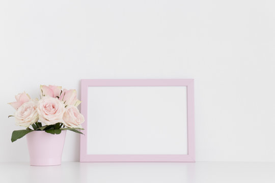 Pink frame mockup with roses in a pot on a white table.Landscape orientation.