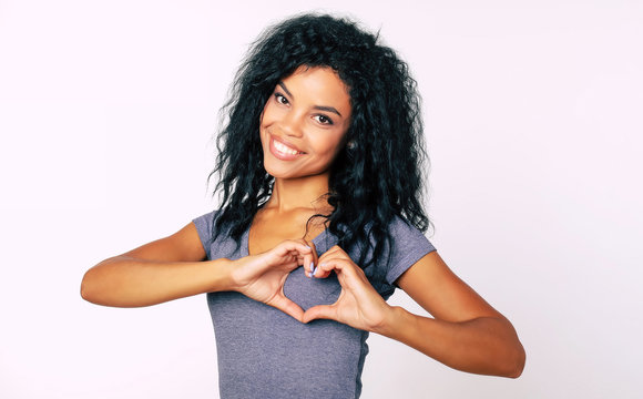 Thank you! Close-up portrait of content Afro ethnic girl with messy raven black hair standing smiling broadly, with her palms near her chest showing a hand heart.