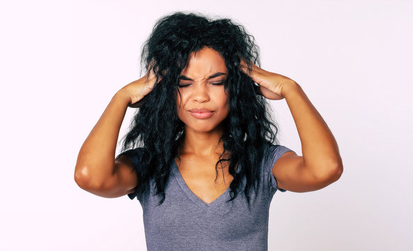 Feeling overwhelmed. Close-up photo of stressed African American woman standing in front of the camera with her hands touching temples indicating headache or nervousness.