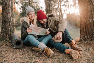 Travel couple camping with map having fun in the forest. Concept of trekking, adventure and seasonal vacation.