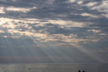 The rays of the summer sun make their way through the thick clouds over the sea