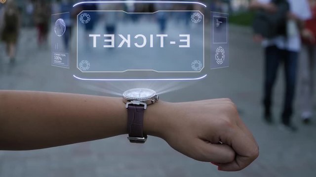 Female hand with futuristic smartwatch shows HUD hologram with text E-ticket. Woman uses holographic technology of future on wristwatch against background of evening city with people