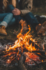 Traveler couple camping in the forest and relaxing near campfire after a hard day. Concept of trekking, adventure and seasonal vacation. - obrazy, fototapety, plakaty