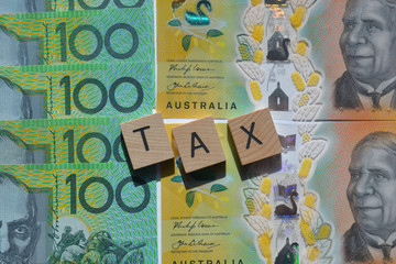 Tax in 3d wooden alphabet letters on a background of Australian one hundred dollar banknotes.
