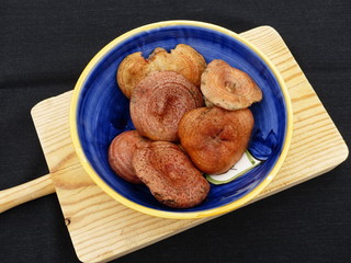 Mushrooms inside a blue ceramic bowl on a wooden table with a black background.