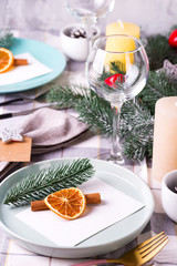 estive Christmas and New Year table setting with dry orange and cinnamon on a gray textile. Dining place decorated with pine cones, branches and candles