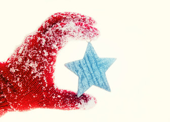 Hand in red gloves holds a small wooden star, Christmas toy on a light background
