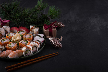 Assorted sushi sashimi set with salmon, tuna and eel on dark slate background with decorations. Christmas or New Year background. Tree branch with gifts. Traditional japanese food. Copy space for text