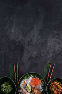 Assorted sushi set on dark slate background. Wakame, seafood salad, salmon, scallop, eel and prawn sashimi served with daikon radish. Vertical, copy space for text. Restaurant menu. Traditional  food