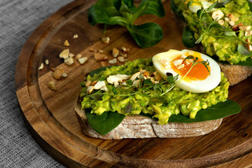 Avocado toast with soft boiled egg, herbs, spinach and nuts on a wooden board. Healthy food concept. Healthy breakfast