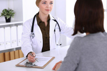 Young woman doctor and patient at medical examination in hospital office. Khaki colored blouse of therapist looks good. Medicine, healthcare and doctor's appointment concept